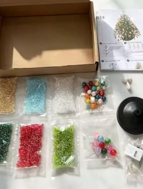 Caixa aberta ao lado de saquinhos de pérolas coloridas, enfeites e base.
